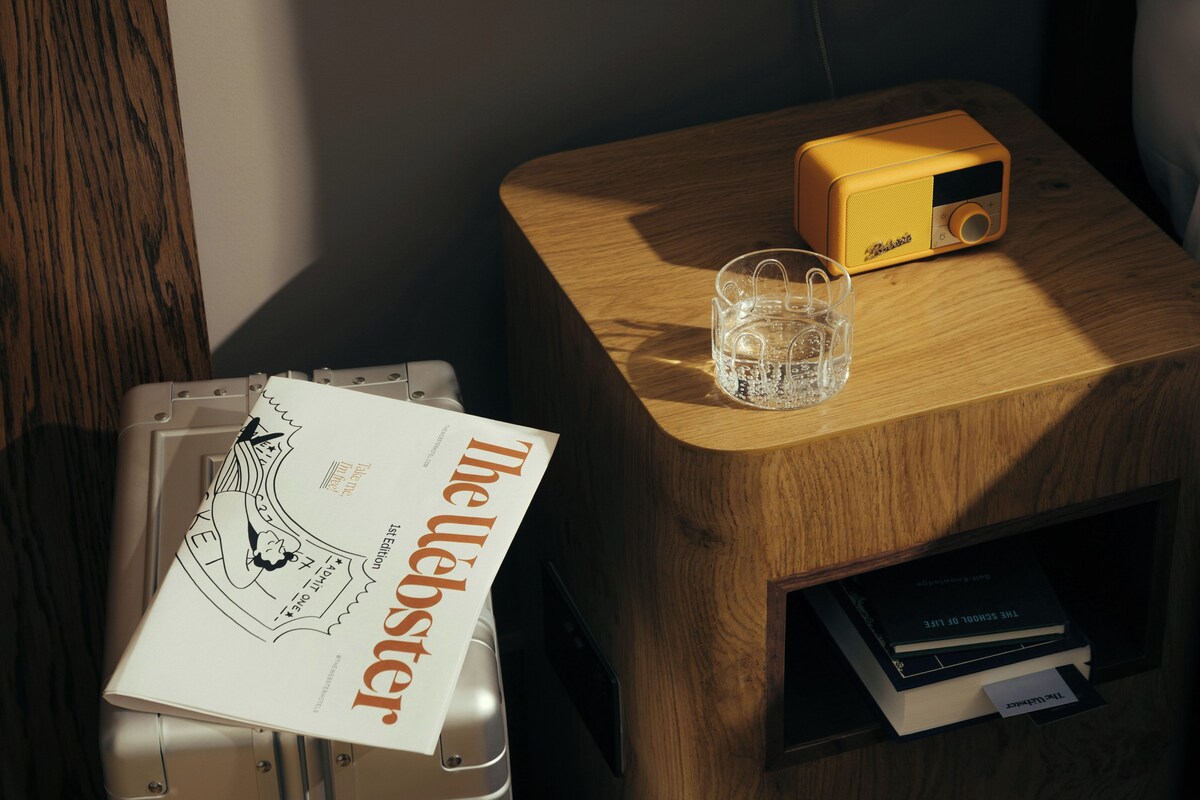 A wooden side table with a radio, a glass of water, and a book titled 'The Leblancster'.