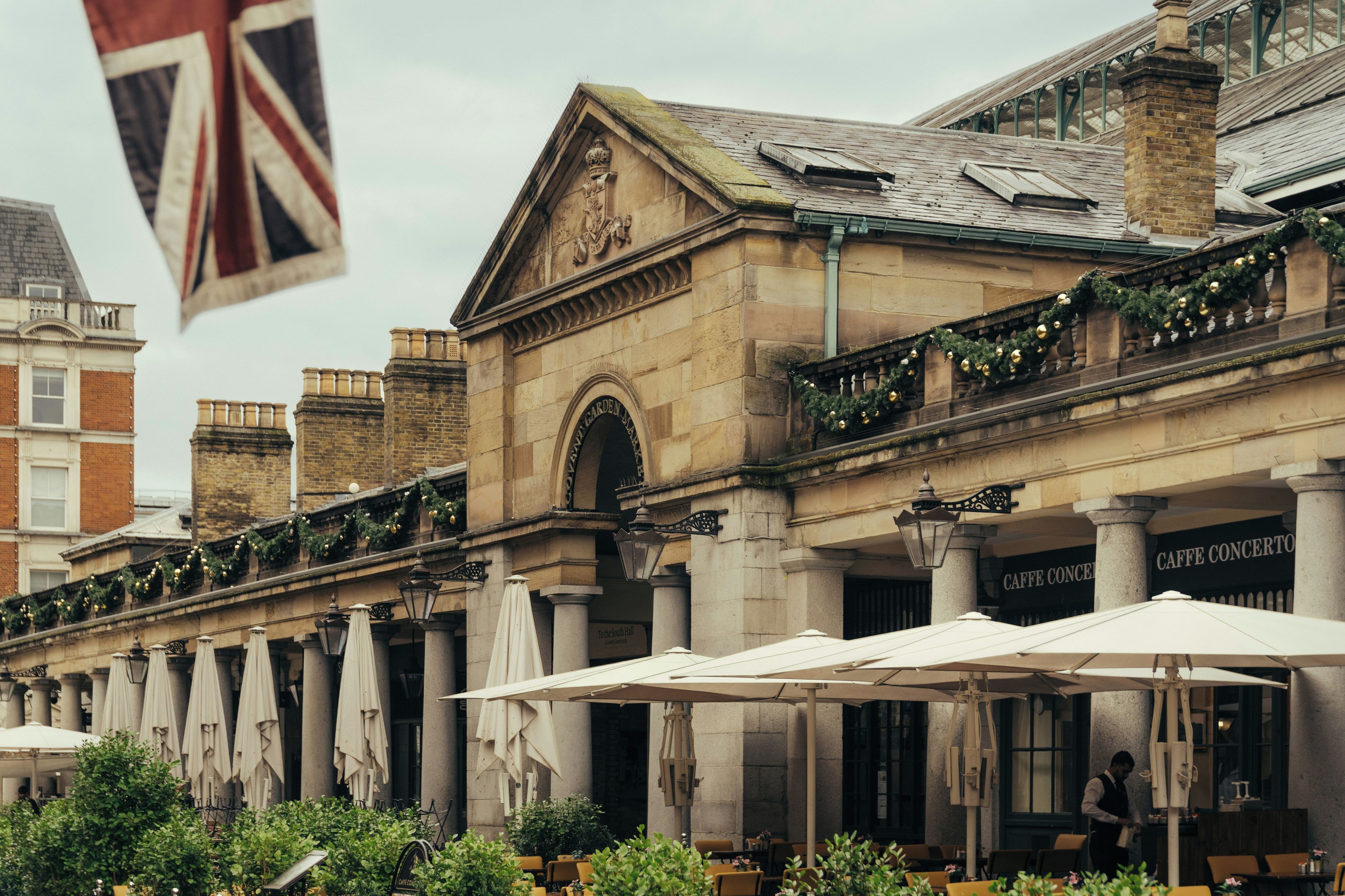 A historic building with a classical facade, outdoor seating with umbrellas, and a flag.