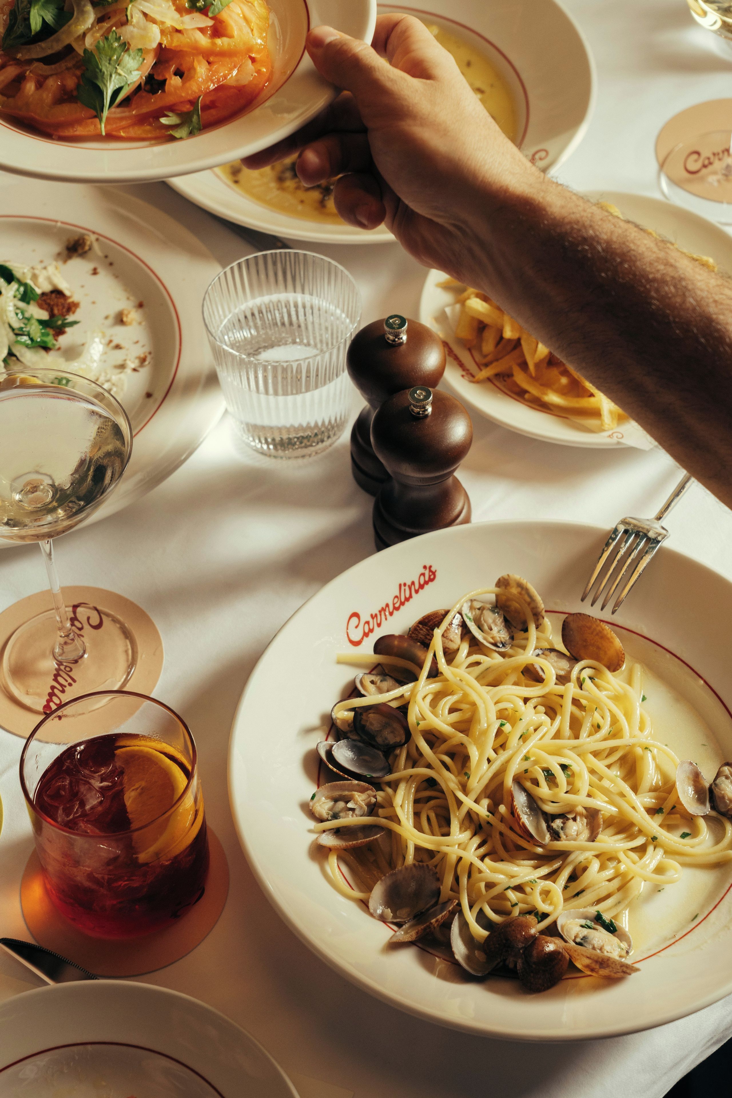 A dining table with plates of pasta, a glass of water, and a glass of red beverage.