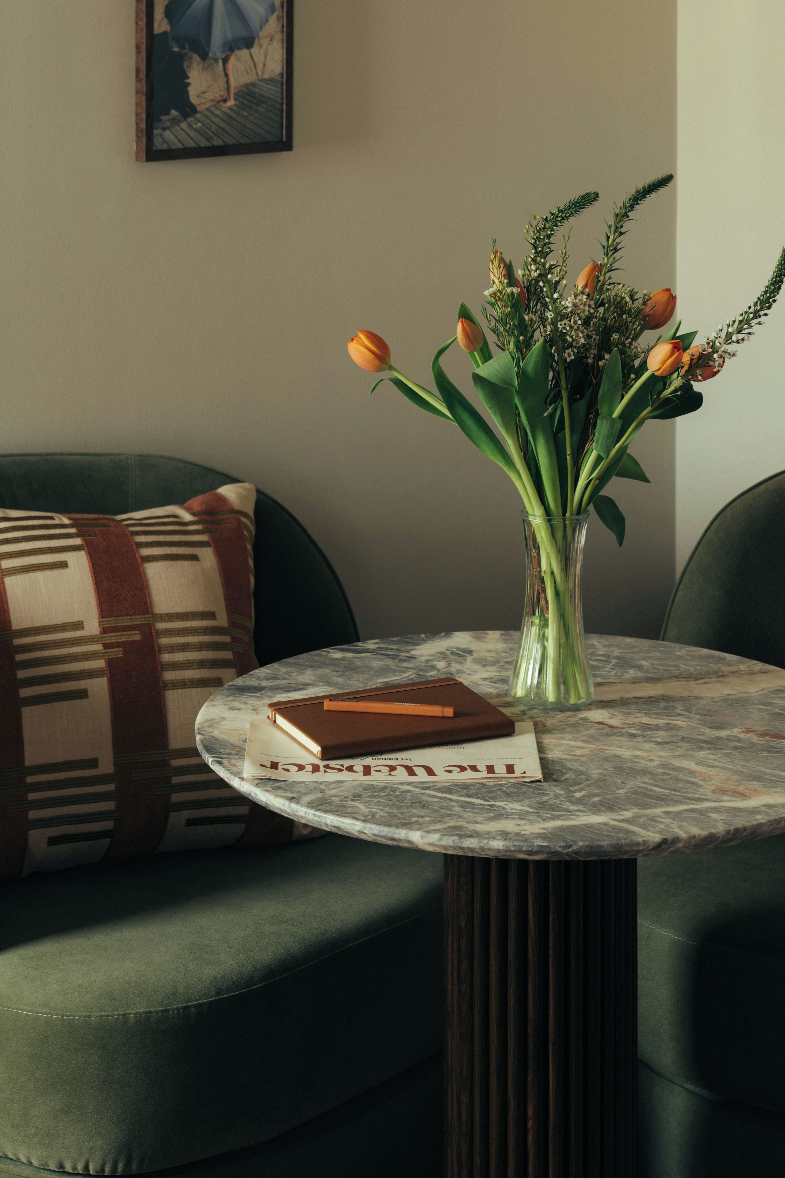 A round table with a vase of flowers, a book, and a cushion on a green sofa.