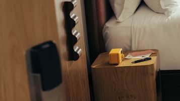 Una mano abriendo una puerta, una mesita de noche con una lámpara y una cama con almohadas.