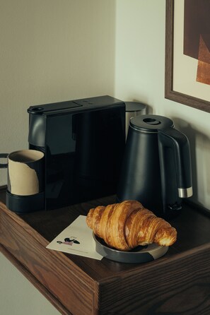 A coffee maker, a croissant, and a framed picture on a wooden surface. - The Webster Covent Garden – New Lifestyle Hotel – £60 Food & Drink Credit per Stay (London)