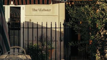 Un área de estar al aire libre con mesas y sillas, un toldo a rayas y un letrero que dice 'The Webster'.