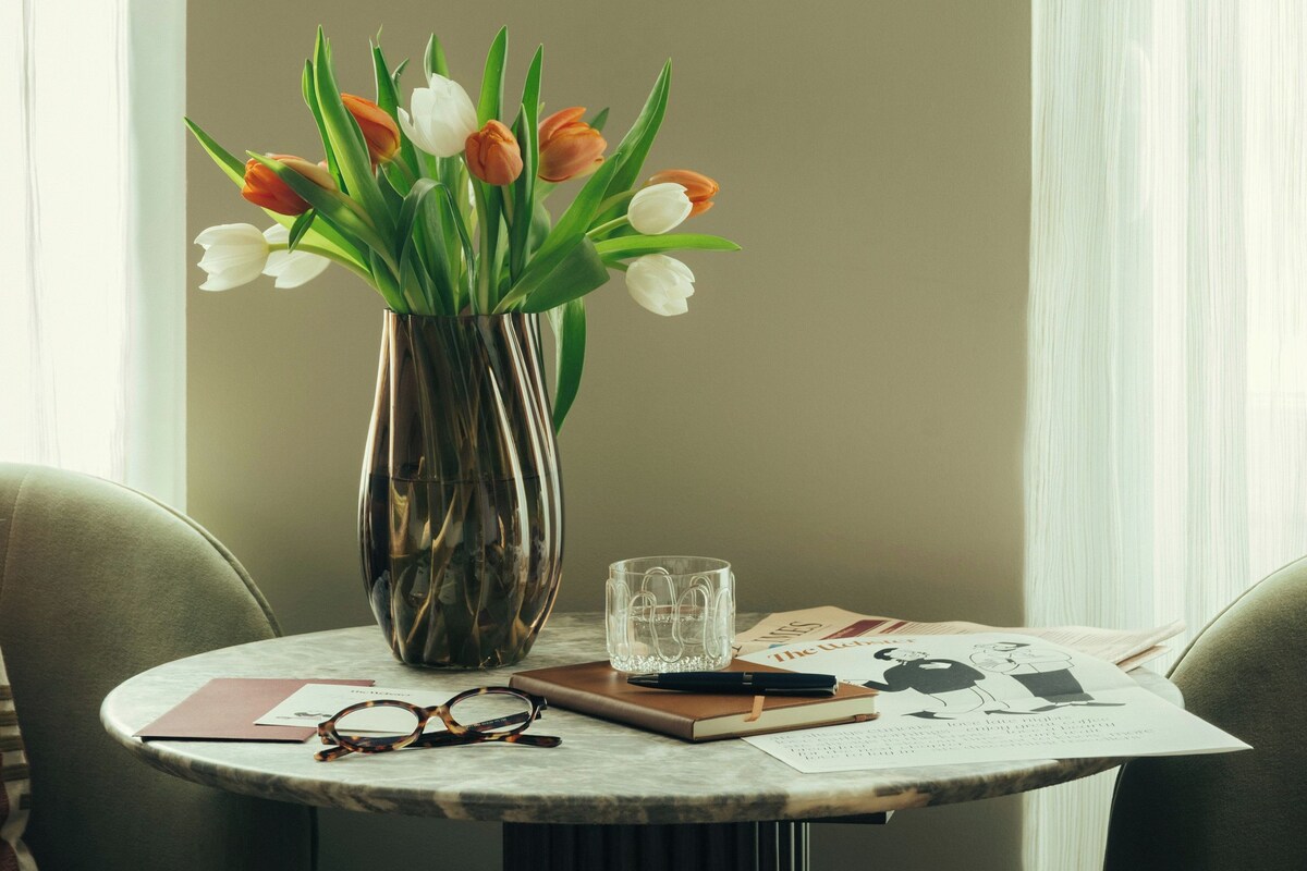A round table with a vase of tulips, a pair of glasses, a notebook, and a glass.