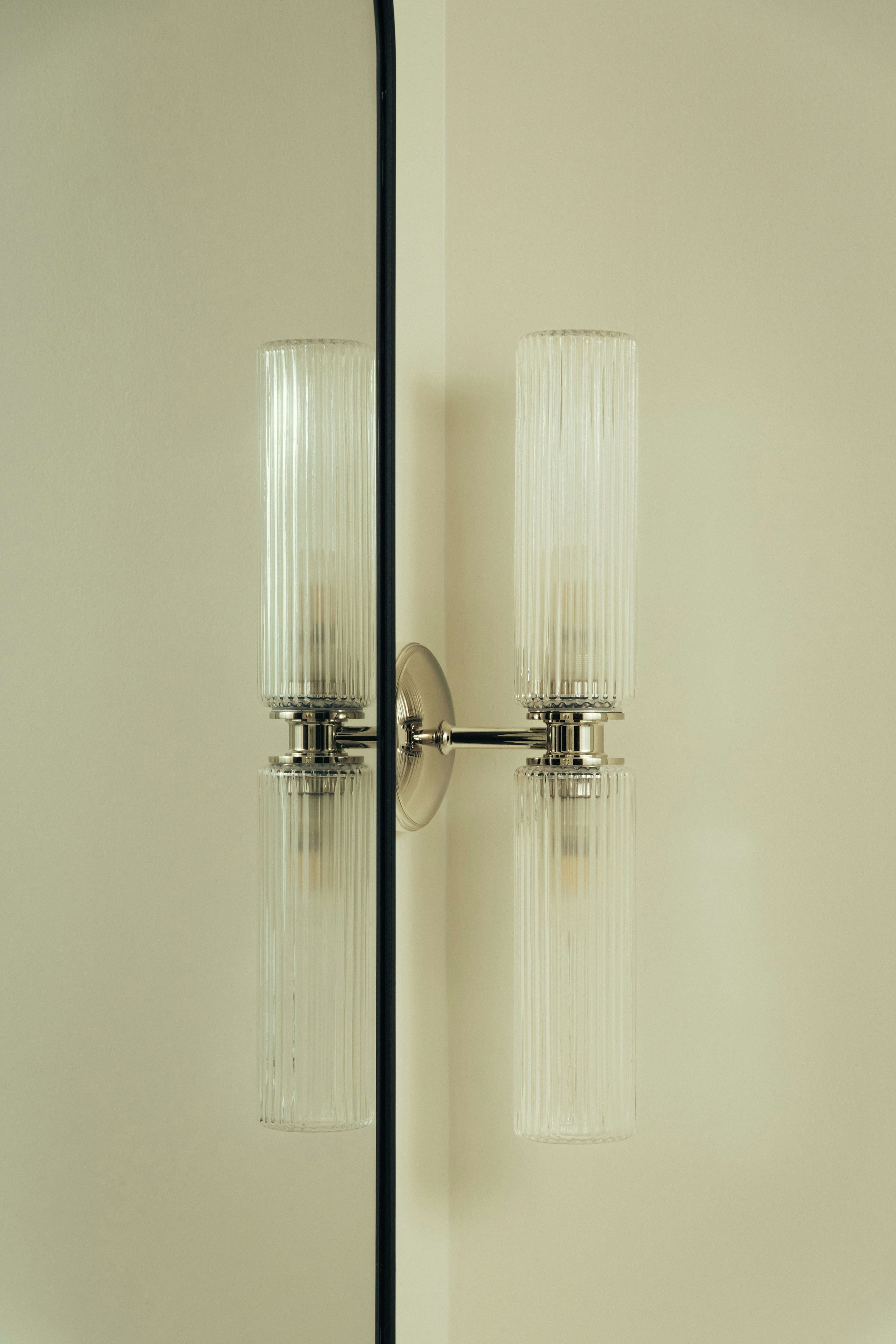 A wall-mounted light fixture with two clear glass shades and a metallic base.