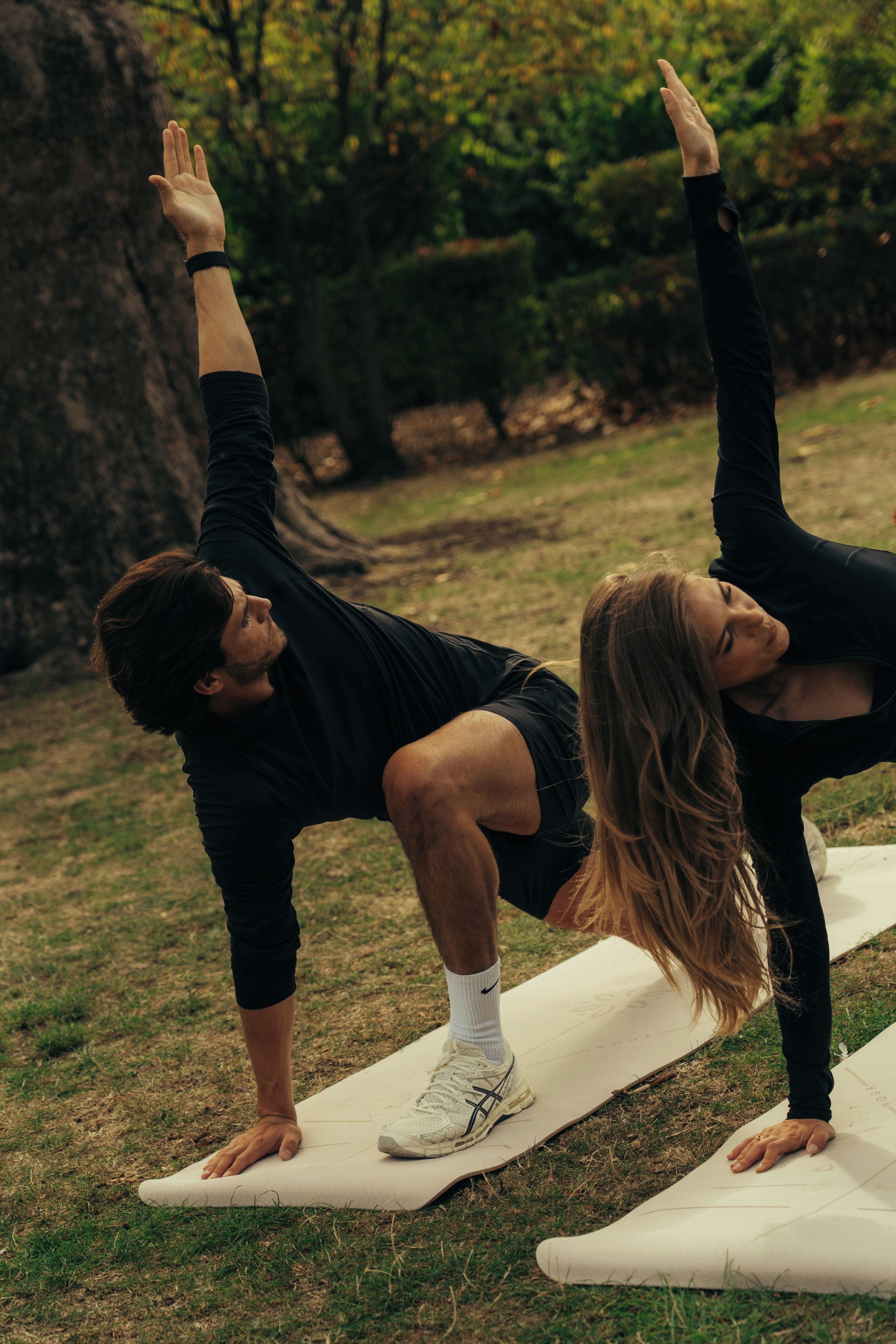 Dos personas practicando yoga sobre esterillas al aire libre.