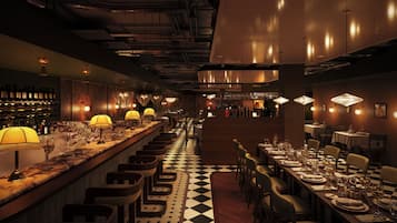 A bar area with a checkered floor, bar stools, and a wine display.