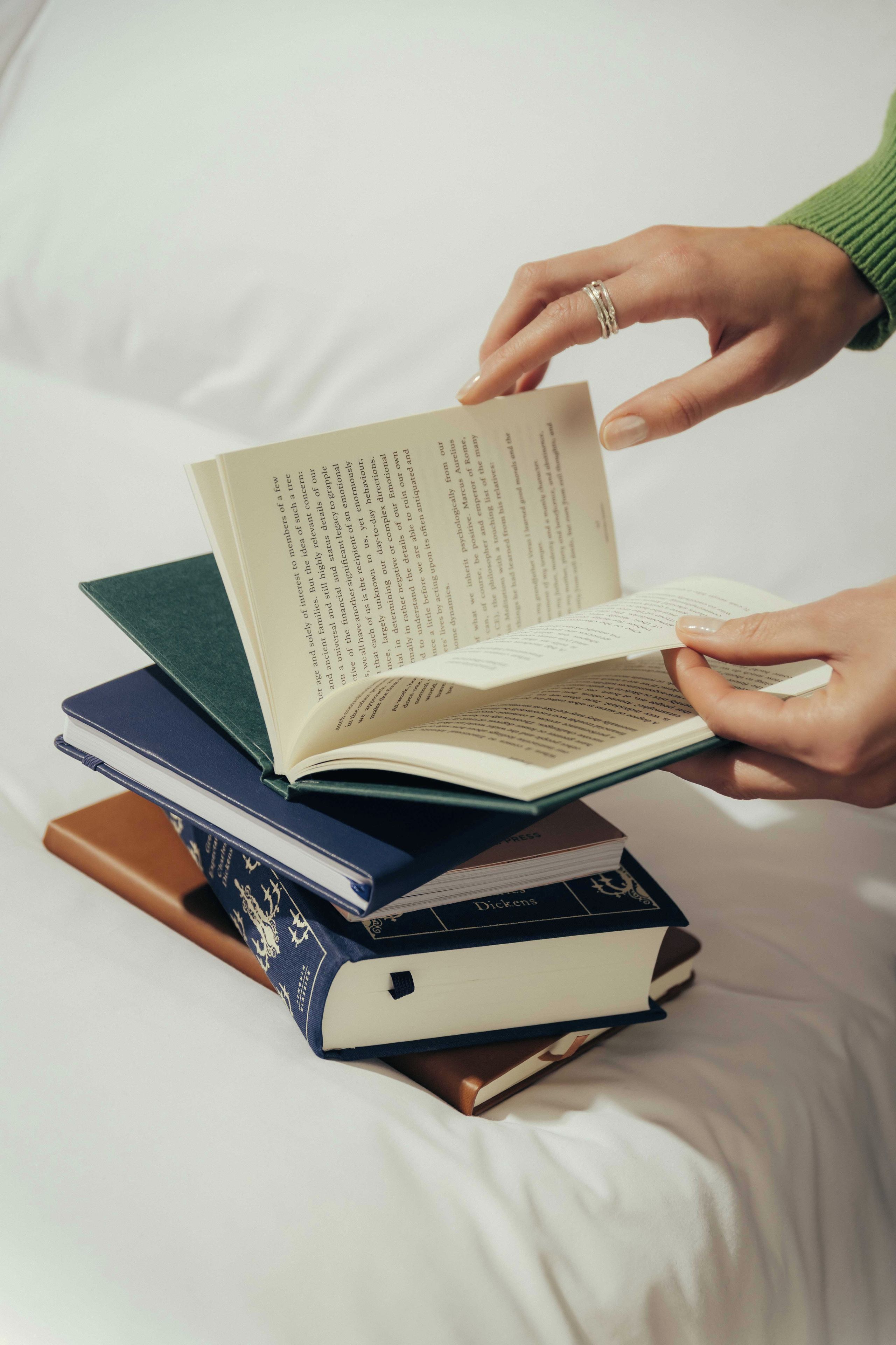 A person holding an open book with a stack of books underneath.