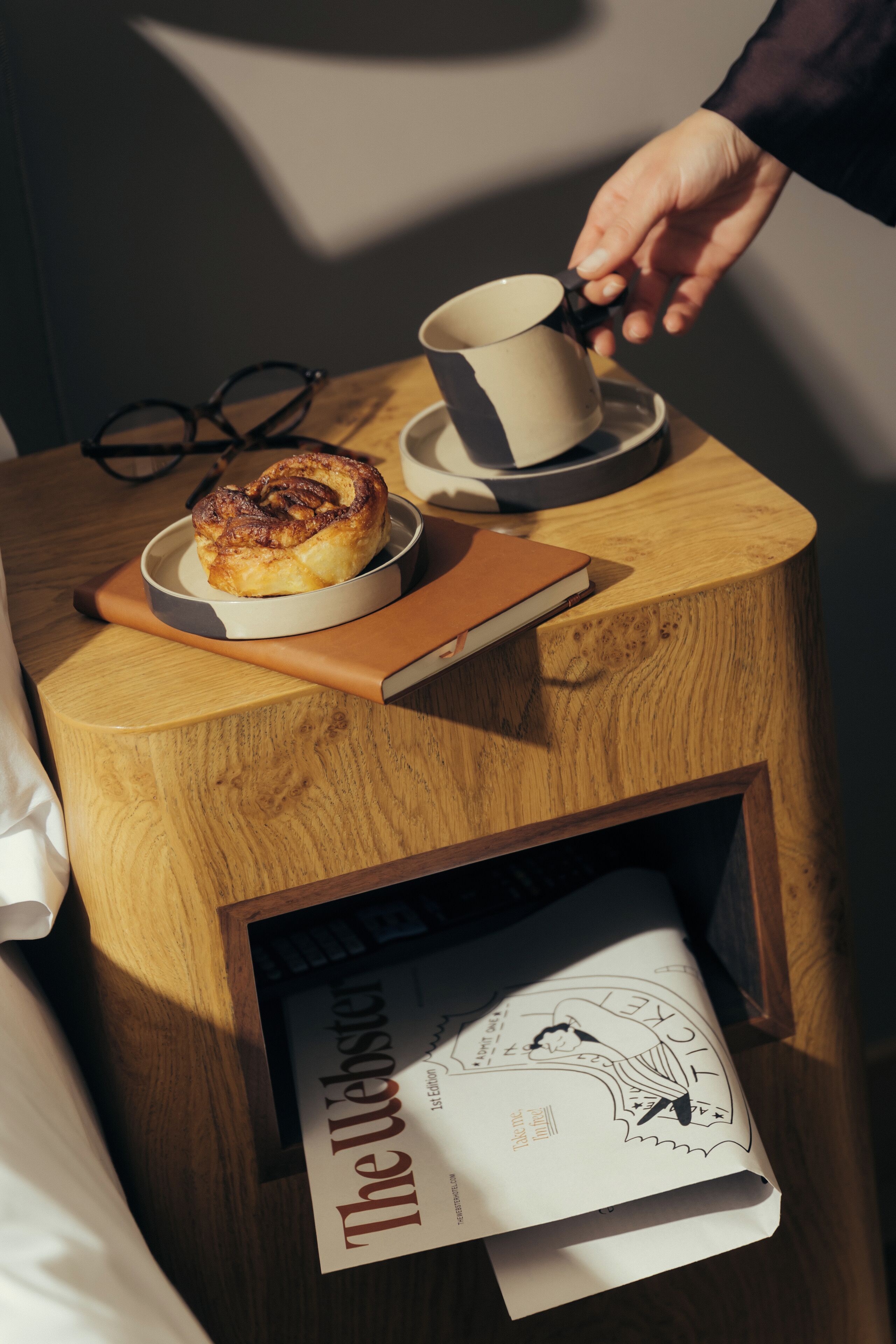 A wooden side table with a cup, a book, and a pastry.