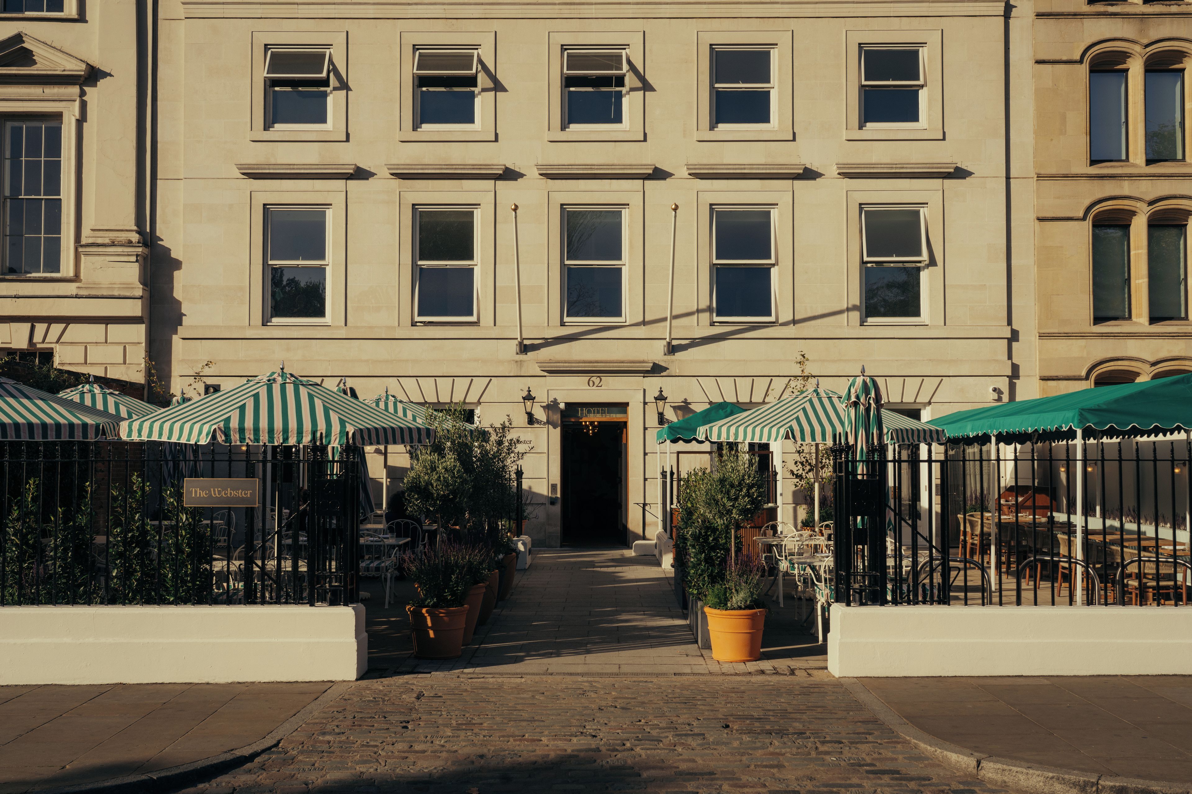 A building with a central entrance, multiple windows, and outdoor seating with striped umbrellas.