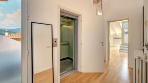 A hallway with a wooden floor, a door leading to a room with a green wall, and a view of a building with a tiled roof. - Penthouse with Private Terrace (Como)