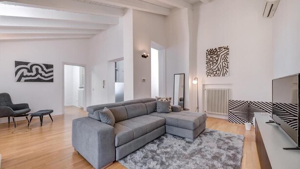 A modern living room with a grey sectional sofa, a small black chair, and a grey rug. There is a flat-screen TV on a stand to the right. - Penthouse with Private Terrace (Como)