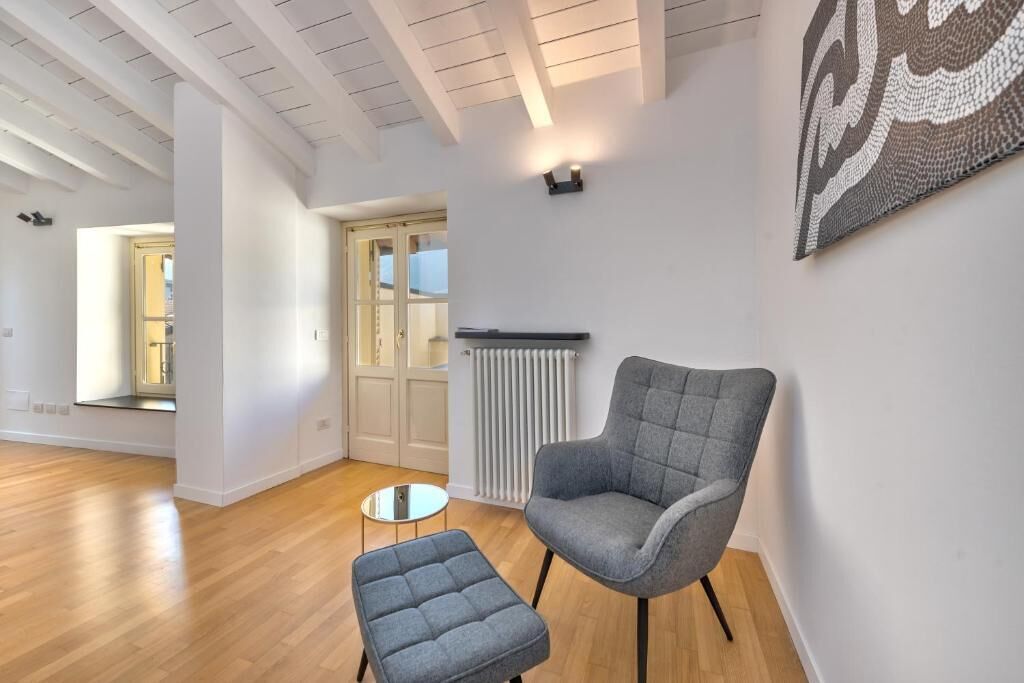 Un salon moderne avec un fauteuil et un pouf gris, un plancher en bois, un radiateur blanc et une décoration murale à motifs.