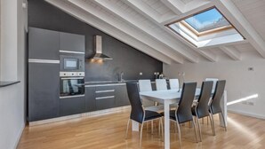 A modern kitchen with a skylight, a dining area with a white table and black chairs, and wooden flooring. - Penthouse with Private Terrace (Como)