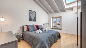 A modern bedroom with a large bed, a skylight, a view of the city, and a bedside table with a lamp. - Penthouse with Private Terrace (Como)