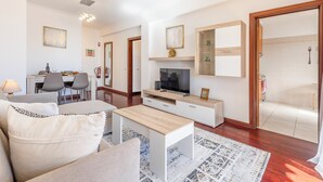 A modern living room with a sofa, coffee table, TV, and dining area. - BoLina 2 bedroom apartment located in the historic center of Caniço. (Caniço)