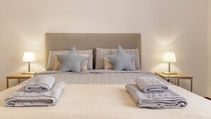 A neatly made bed with a striped bedspread and two pillows, two bedside lamps, and folded towels on the bed. - BoLina 2 bedroom apartment located in the historic center of Caniço. (Caniço)
