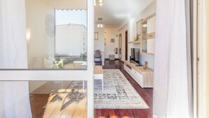 A modern interior with a wooden floor, a patterned rug, a dining area with a table and chairs, and a kitchen with a TV and cabinets. - BoLina 2 bedroom apartment located in the historic center of Caniço. (Caniço)