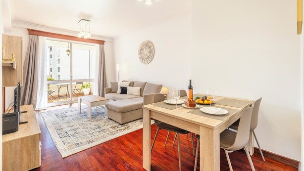 A modern living room with a dining area, a sofa, a coffee table, and a TV on a wooden stand. - BoLina 2 bedroom apartment located in the historic center of Caniço. (Caniço)