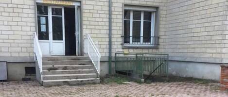Un edificio con fachada de ladrillo, una escalera que lleva a una puerta y un patio empedrado.