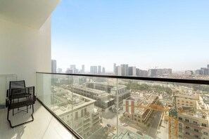 A high-rise balcony with a clear view of the cityscape, a glass railing, and a black chair. - Silkhaus Cozy 1bdr Binghatti Tulip JVC (Dubai)