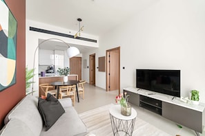 A modern living room with a sofa, a coffee table, and a TV. There is a dining area with a table and chairs, and a kitchen in the background. - Silkhaus Cozy 1bdr Binghatti Tulip JVC (Dubai)