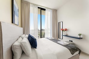 Ein Hotelzimmer mit einem großen Bett, einem Nachttisch mit Lampe, einem Fenster mit Vorhängen und Blick auf die Stadt.