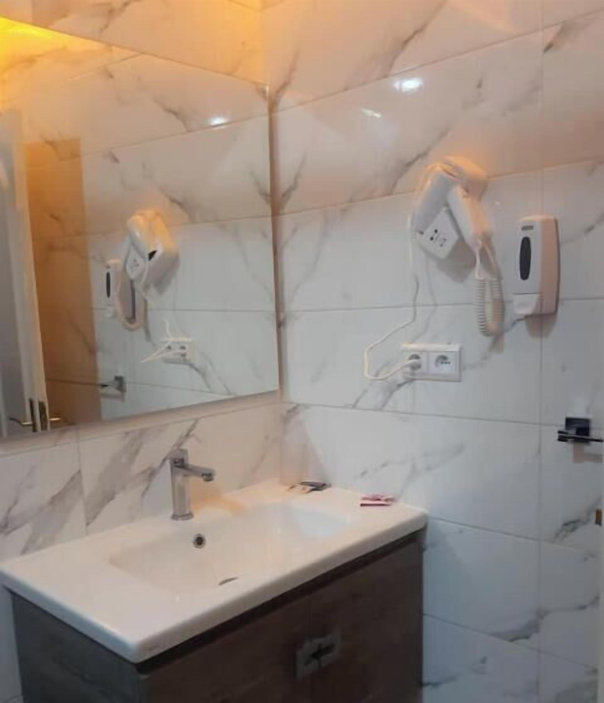 A bathroom with a marble wall, a sink, a mirror, and a hairdryer mounted on the wall.