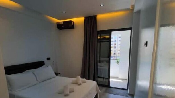 Ein Hotelzimmer mit Bett, einer Glastür zum Balkon und einem kleinen Tisch mit Lampe.