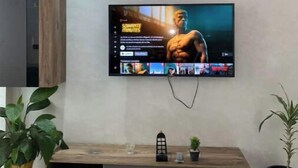 Ein modernes Wohnzimmer mit einem an der Wand befestigten Flachbildfernseher, einer Holzunterhaltungseinheit darunter und zwei Zimmerpflanzen.