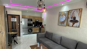 Ein modernes Wohnzimmer mit einem grauen Sofa, einem Holztisch und einer Küche im Hintergrund.