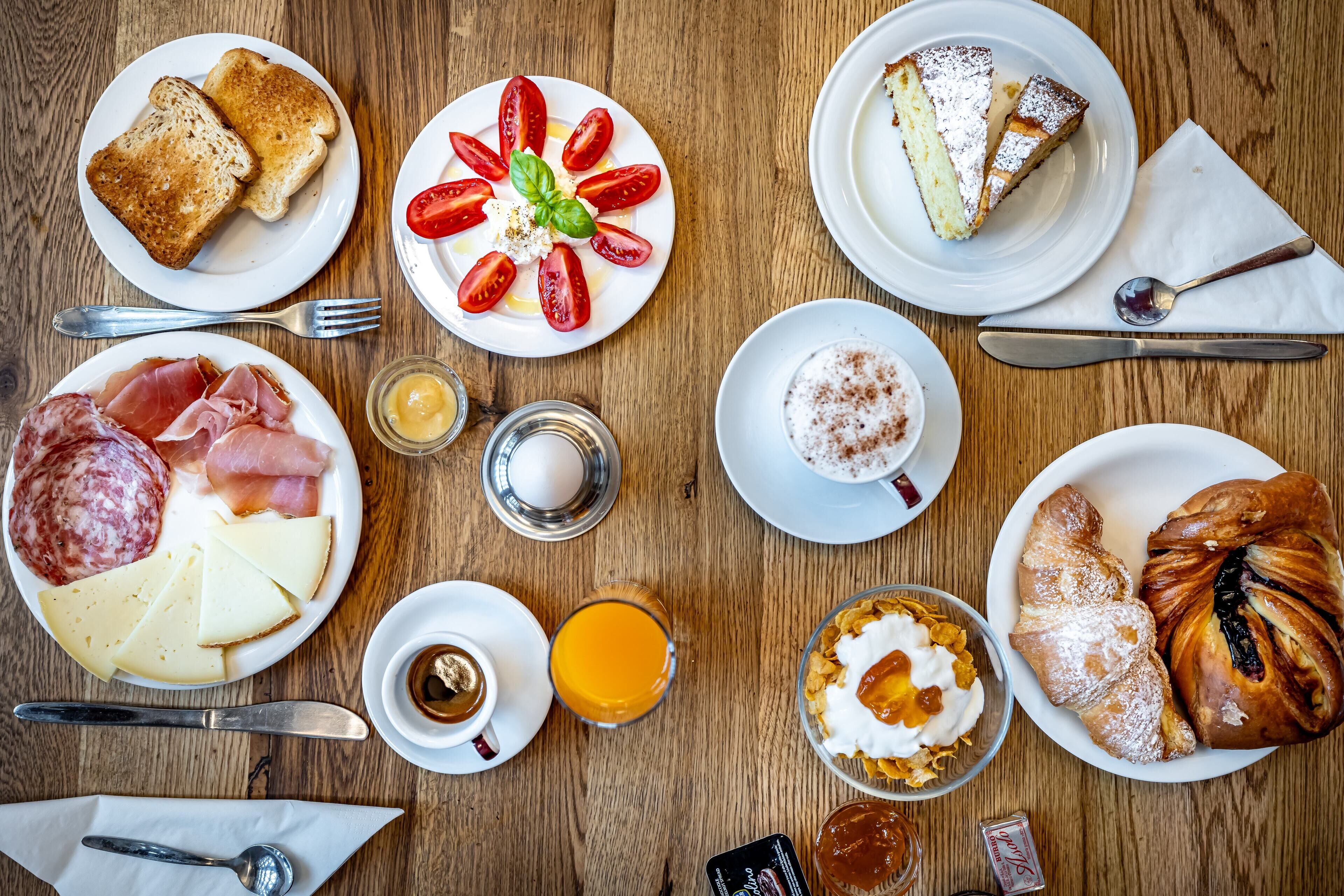 A breakfast spread with toast, cheese, ham, eggs, and pastries on a wooden table.