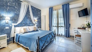 A bedroom with a bed, bedside tables, a desk, a chair, a TV, and a window with curtains. - AGRITURISMO CESANI (San Gimignano)