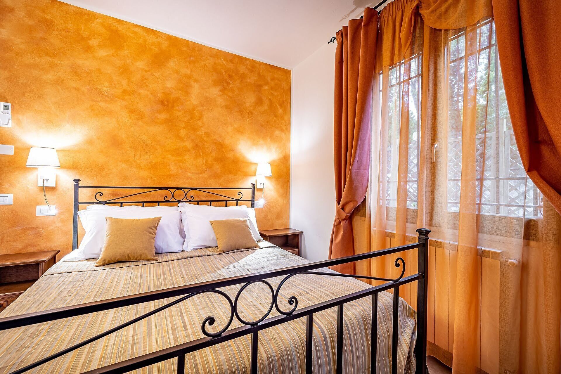 Quarto de hotel com uma cama, duas luminárias de cabeceira, uma janela com cortinas e uma parede com textura.