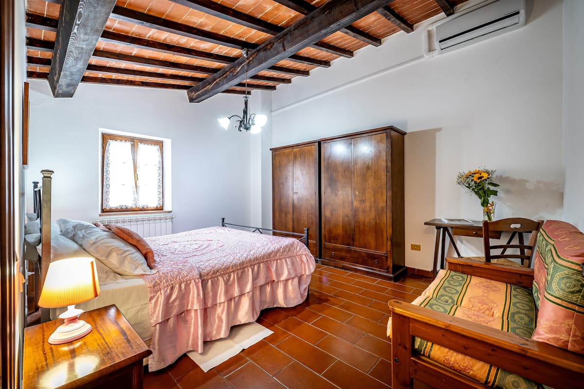 A bedroom with a bed, a wooden wardrobe, a desk with a chair, and a window.