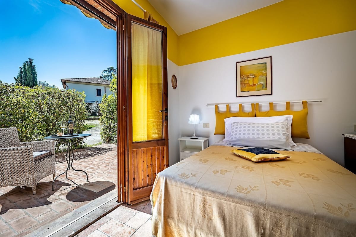 A hotel room with a bed, a nightstand, a lamp, and a view of the garden.