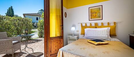 A hotel room with a bed, a nightstand, a lamp, and a view of the garden.