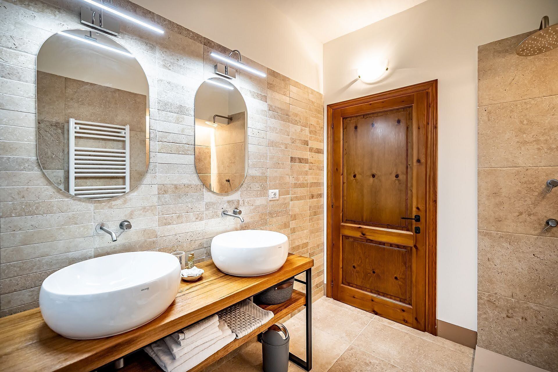A bathroom with two sinks, a wooden vanity, a mirror, and a wooden door.