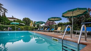 A swimming pool with clear blue water, surrounded by lounge chairs and umbrellas. - AGRITURISMO CESANI (San Gimignano)