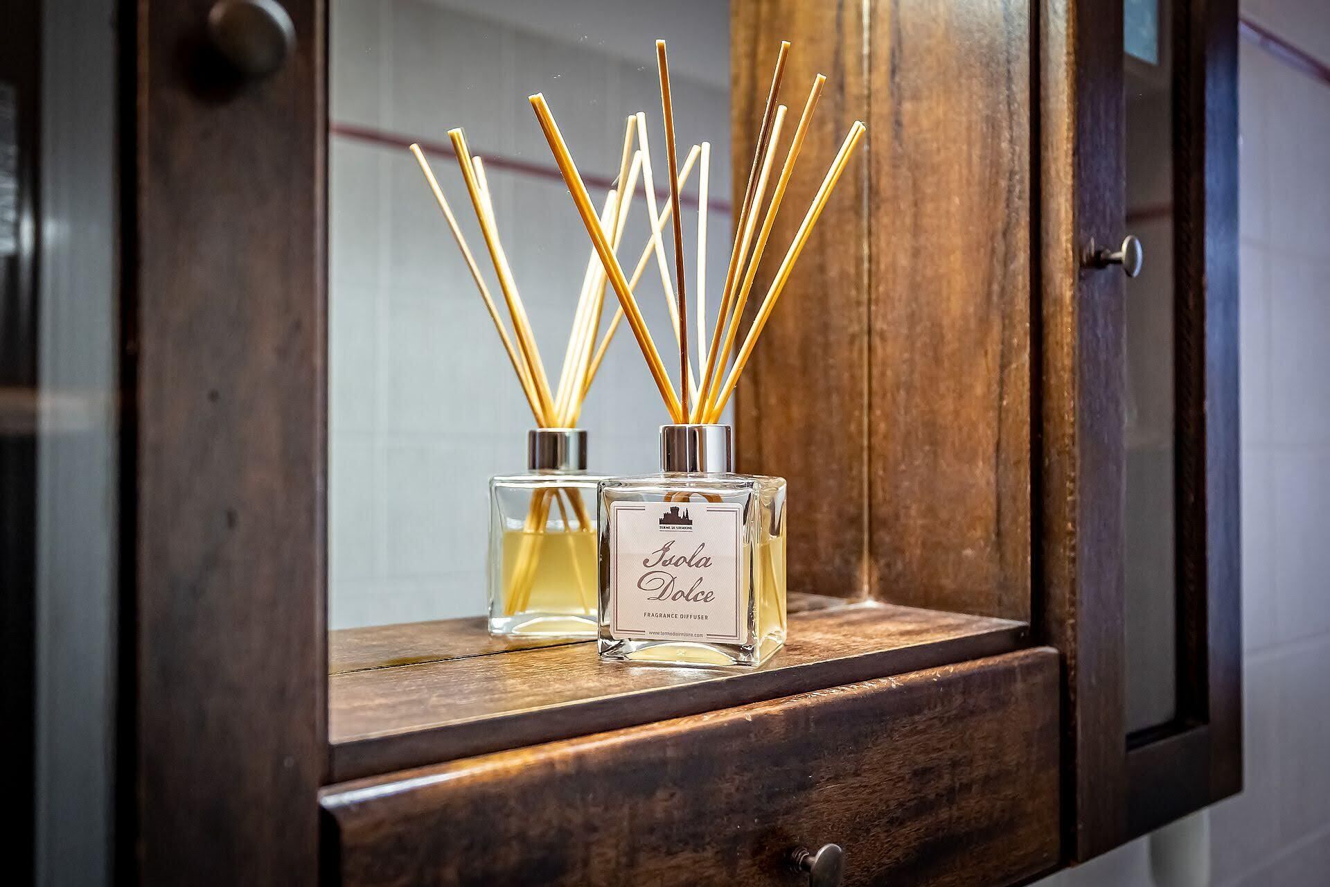 Two glass bottles of fragrance diffuser with reed sticks on a wooden cabinet shelf.