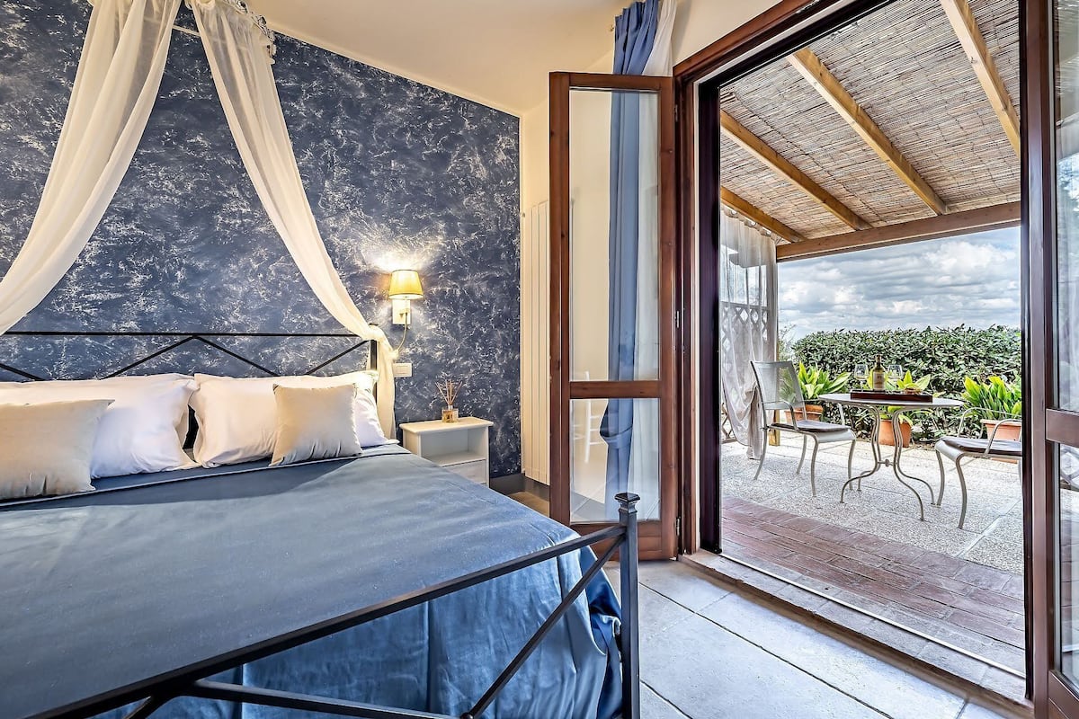 A bedroom with a bed, a nightstand, a lamp, and a view of the outdoor patio area.