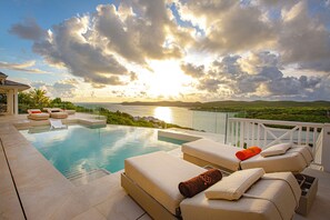 A poolside area with lounge chairs and a view of the sea at sunset.