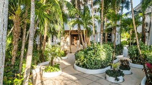 Une cour intérieure agrémentée de palmiers, un chemin central et des jardinières blanches contenant différentes espèces de plantes.