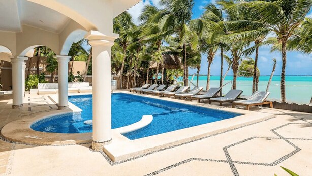 Un espace piscine avec des chaises longues, des palmiers et une vue sur l’océan.
