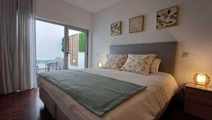 Ein Schlafzimmer mit einem großen Bett, einem Nachttisch, einer Wandlampe und einer Glastür, die zu einem Außenbereich führt.