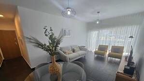 Ein modernes Wohnzimmer mit einem runden Glastisch, grauen Sofas und einer Topfpflanze.