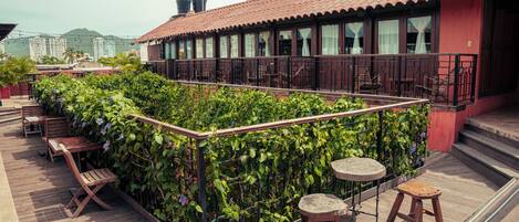 A rooftop terrace with wooden furniture, a climbing plant wall, and a view of buildings in the background.