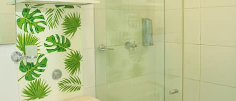 Un baño con inodoro, lavamanos, ducha con puerta de vidrio y repisas con diseño de hojas.