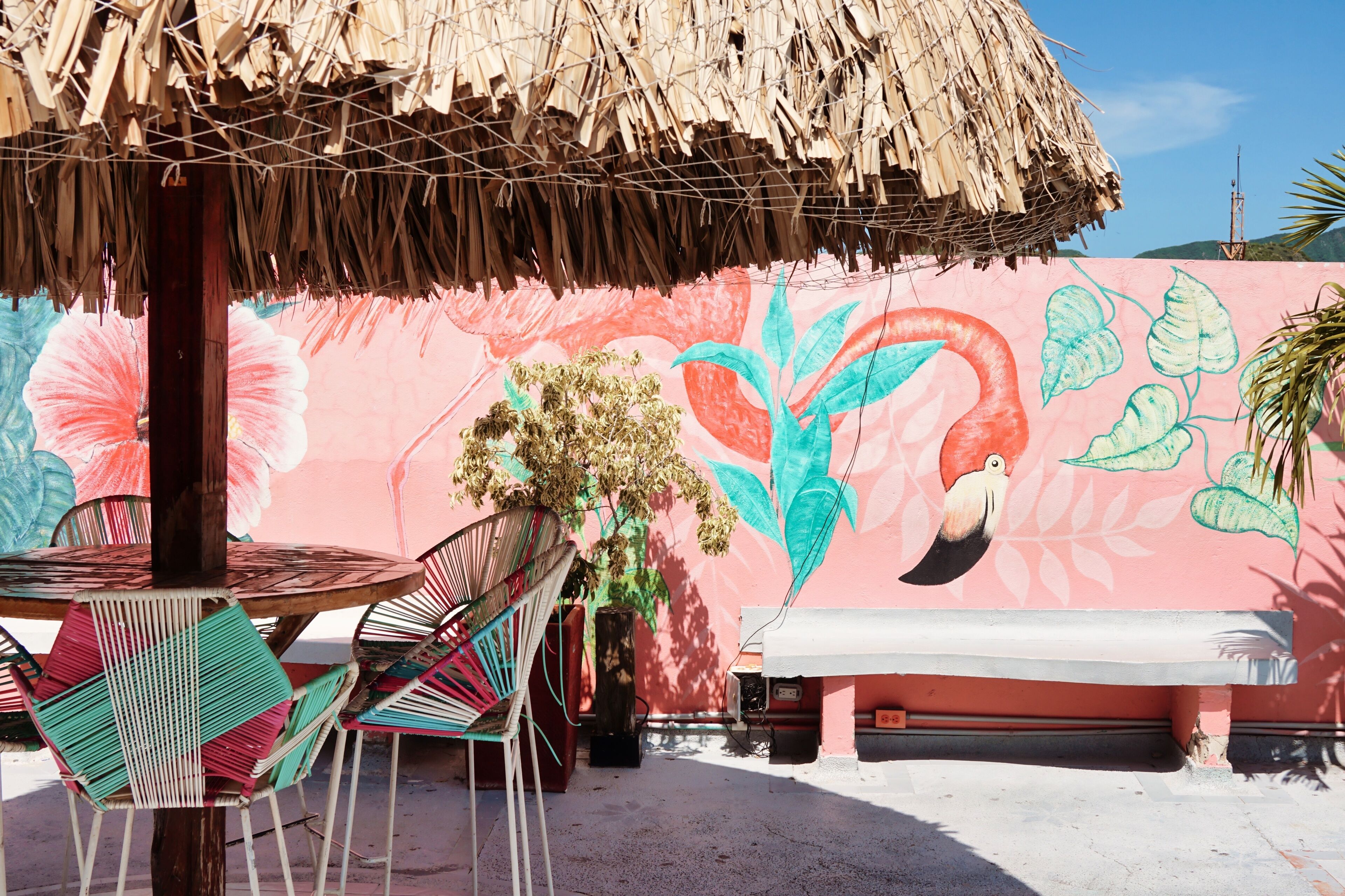 A beachside seating area with a thatched umbrella, a mural with tropical motifs, and a bench.