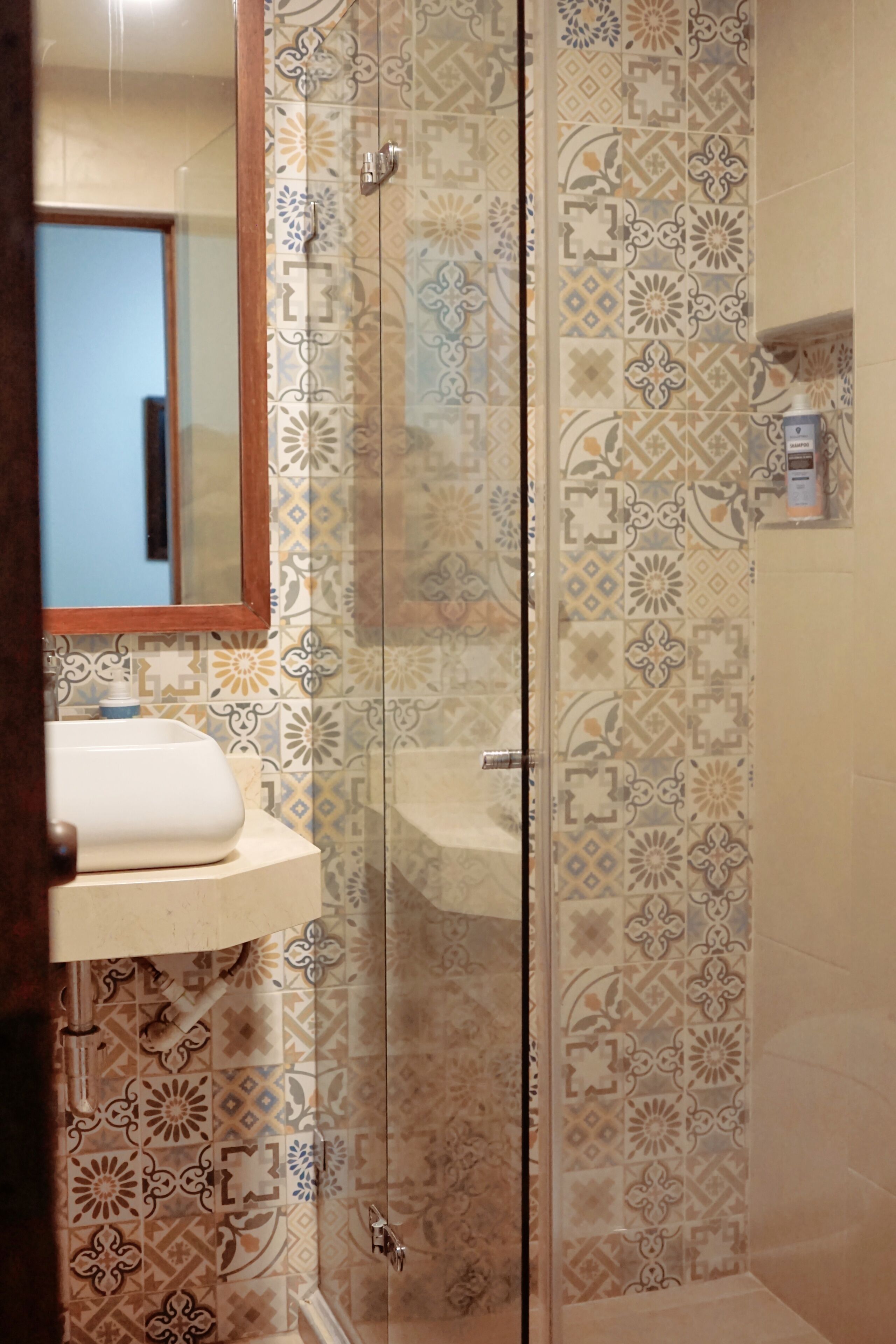 Een badkamer met een douche met glazen wand, een wastafel en tegelwerk met een patroon.